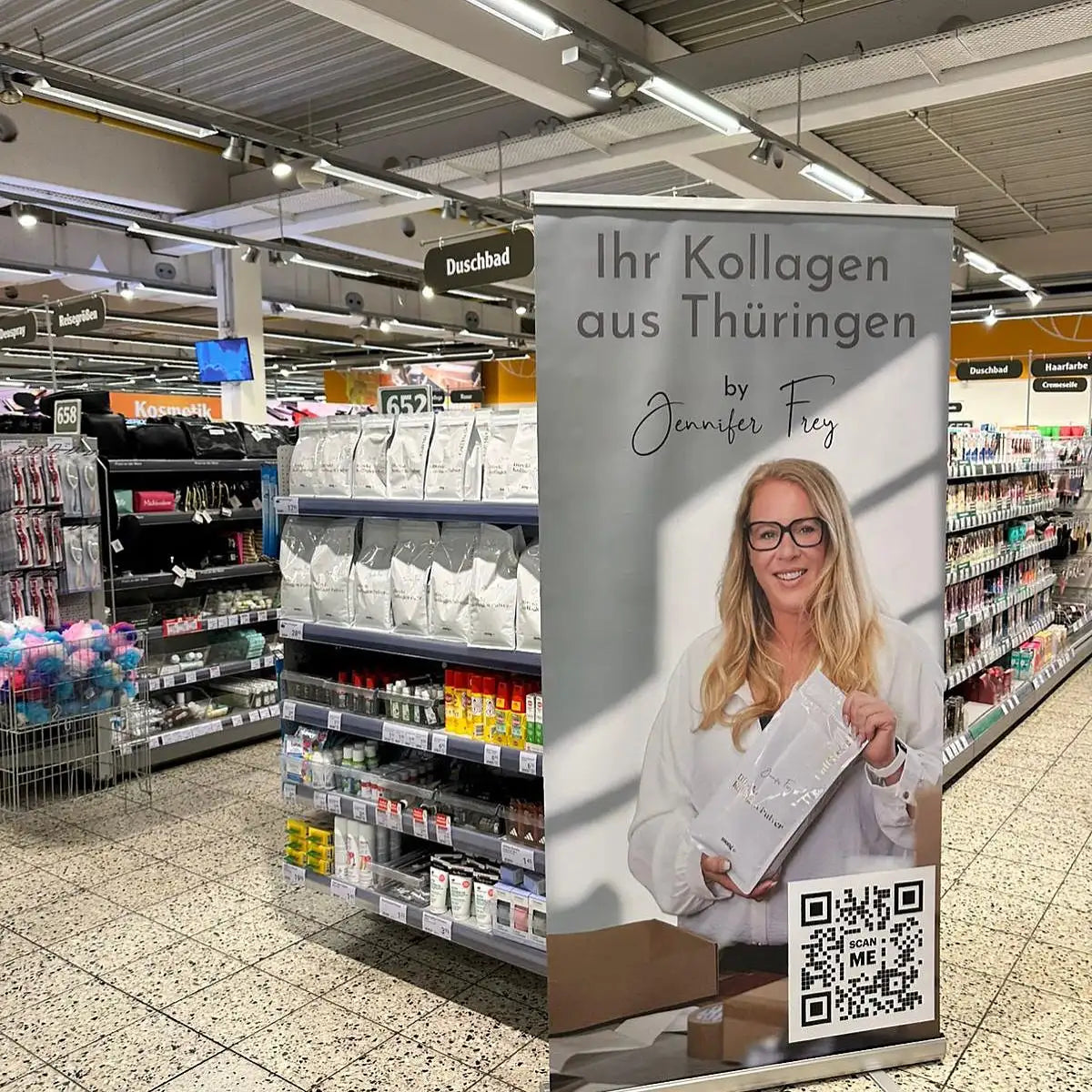 Graues Banner mit einer lächelnden Frau mit Brille, die ein weißes Paket in den Händen hält, mit Text, der „ihr kollagen aus thüringen by jennifer frey“ sagt, und einem QR-Code unten.